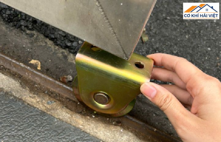 Cận cảnh bánh xe sắt đang trượt trên đường ray V của cửa cổng sắt lùa