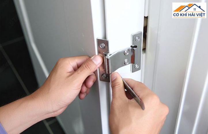 Cận cảnh một chiếc bản lề lá bằng inox đang được lắp trên cánh cửa sắt hộp