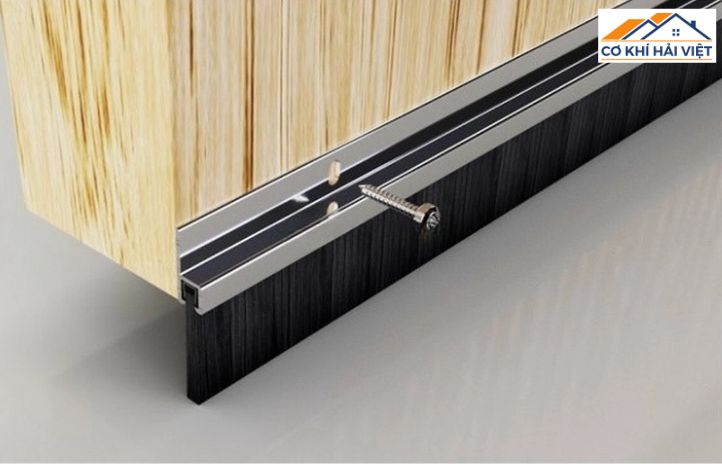 Một thanh nẹp chân cửa có gắn dải lông đang được lắp vào mép dưới của cánh cửa sắt