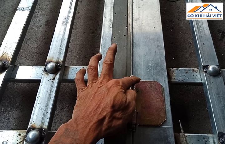 Người thợ cơ khí đang cẩn thận hàn một chiếc bản lề trụ vào khung cửa sắt